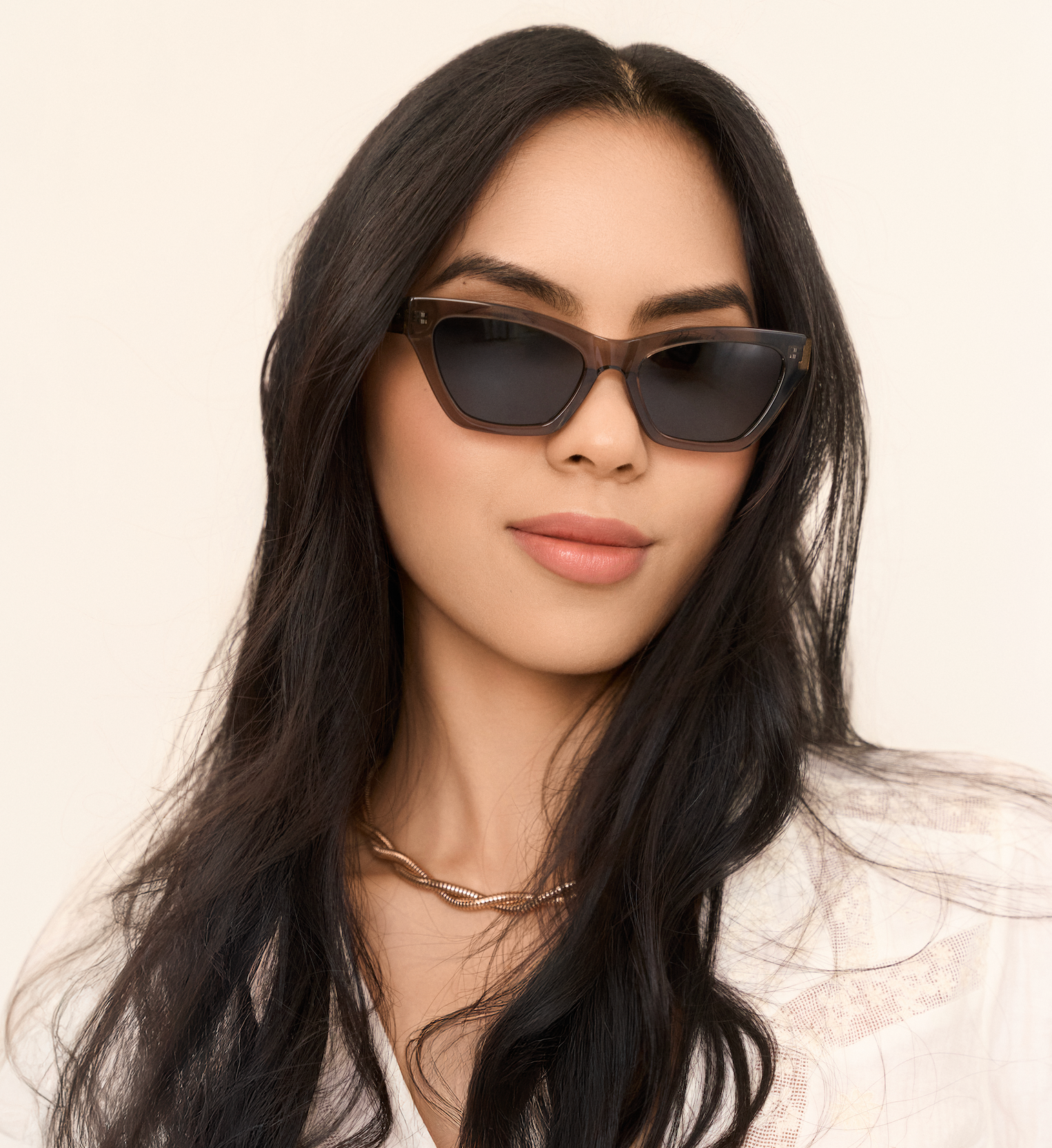 Woman with long dark hair wearing KayTran Eyewears Kai - Sage cat-eye sunglasses and a gold chain necklace.