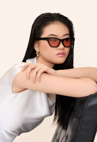 Woman with straight black hair in Kai - Black and Peach sunglasses by KayTran Eyewear, gold earrings, white top.