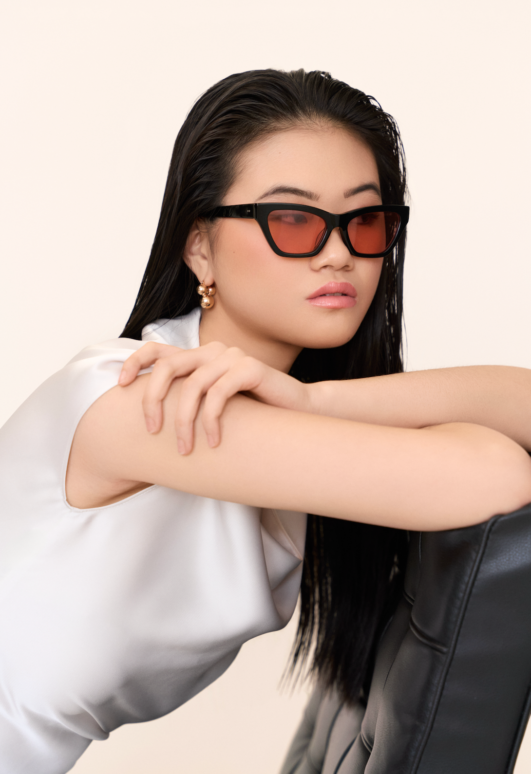 Woman with straight black hair in Kai - Black and Peach sunglasses by KayTran Eyewear, gold earrings, white top.