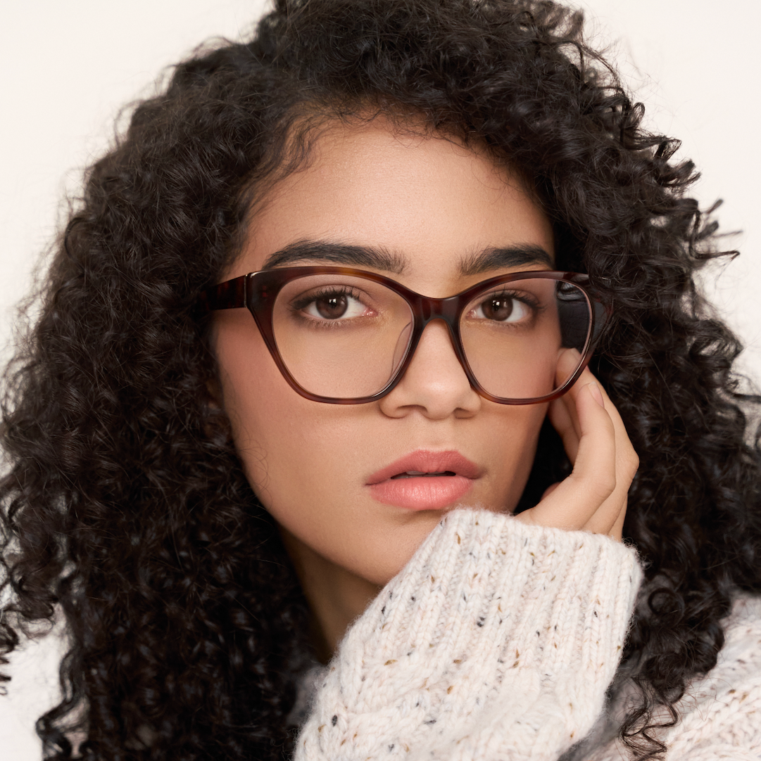 Woman with curly hair wears KayTran Eyewear’s Taylor Optical - Honey Tort glasses and a light knit sweater.
