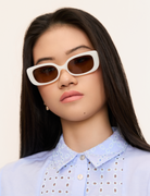 Woman with long dark hair wears KayTran Eyewears Billie - Ivory sunglasses and a light blue collared shirt, facing forward.