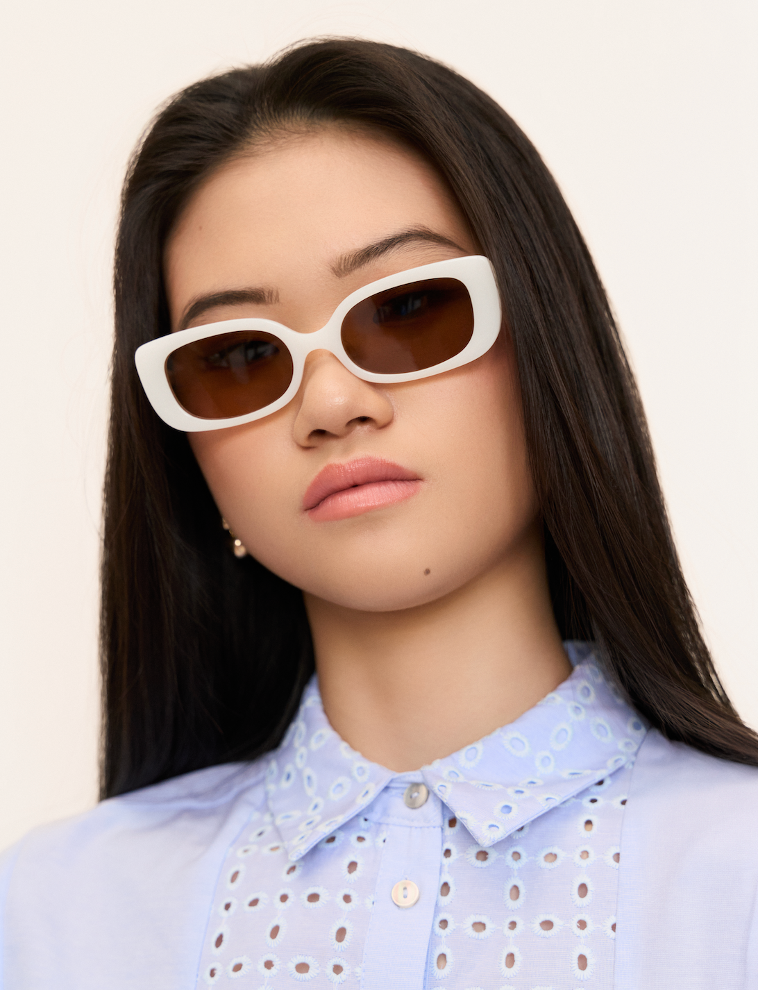 Woman with long dark hair wears KayTran Eyewears Billie - Ivory sunglasses and a light blue collared shirt, facing forward.