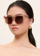 Woman with long dark hair wears KayTran Eyewears Logan - Bloom square sunglasses, looking forward.
