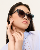 A woman poses with her hands near her face, wearing KayTran Eyewears Harper - Sea Pine cat-eye sunglasses.
