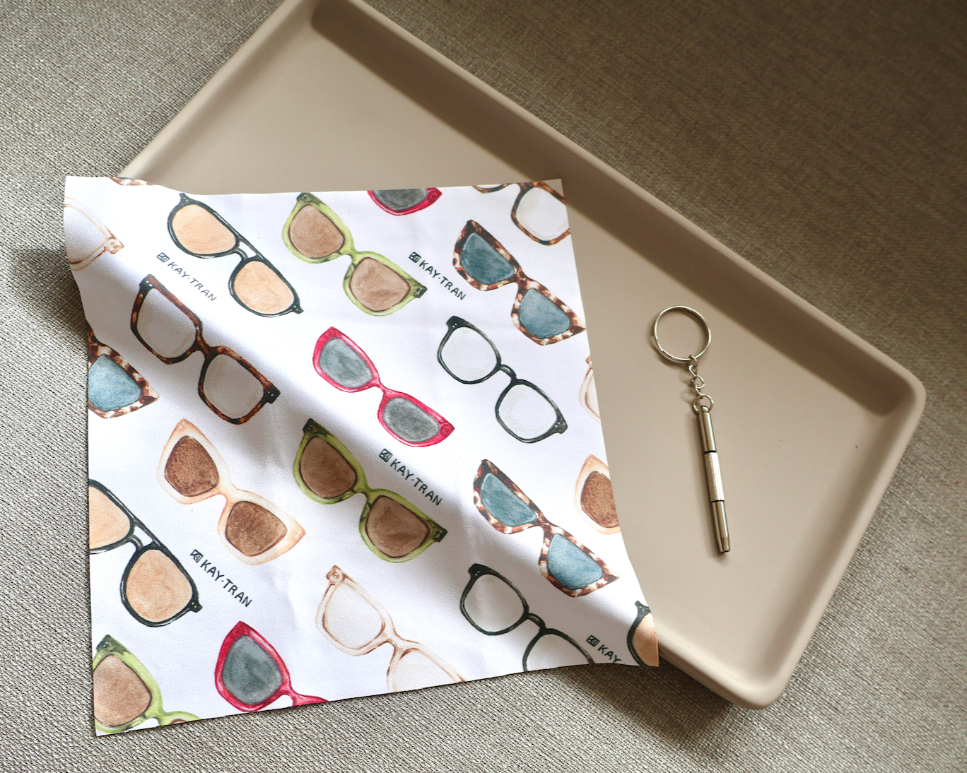 The KayTran x Ton Ton Art Tune Up Kit by KayTran Eyewear rests on a beige tray beside a metal keychain.