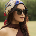 Woman wearing KayTran Eyewear Rowan - Sage sunglasses, a patterned headscarf, and an asymmetrical brown top outdoors.