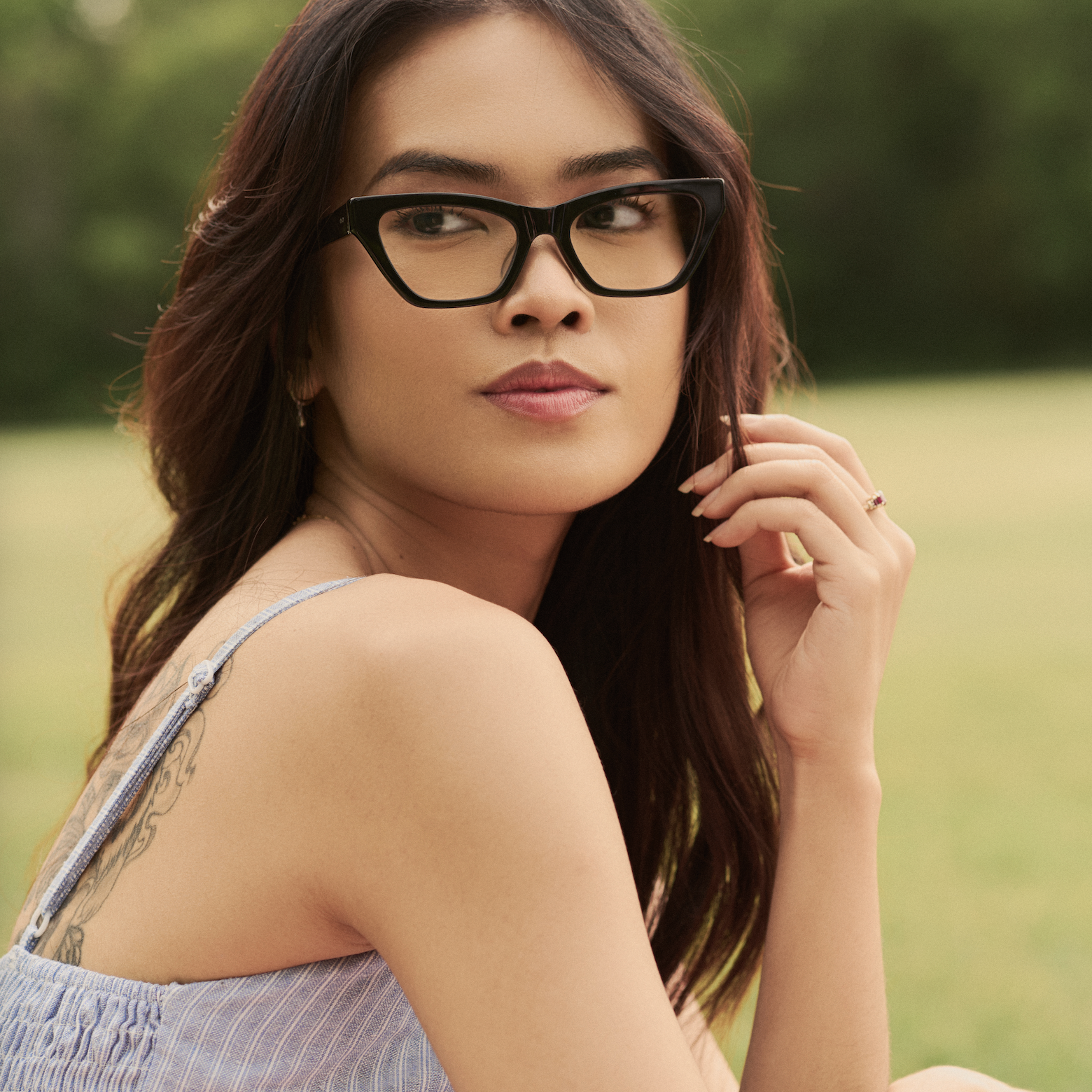 A woman wears KayTran Eyewears Kai Optical - Polished Black glasses outdoors with greenery in the background.