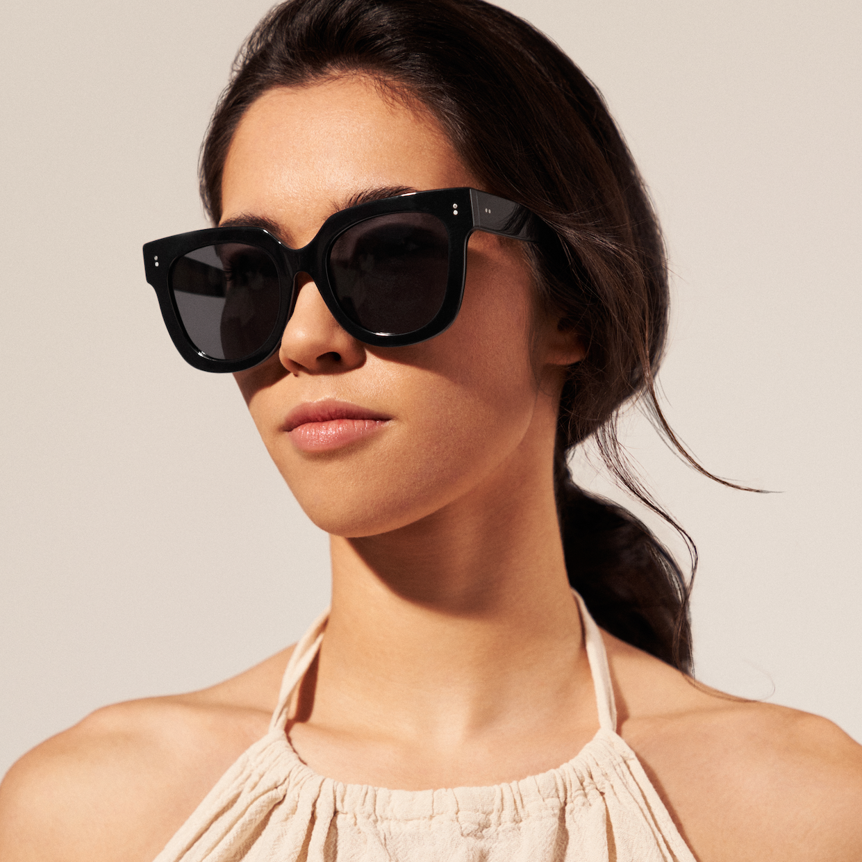 A woman in KayTran Eyewears Rowan - Polished Black sunglasses and a light halter top looks ahead.