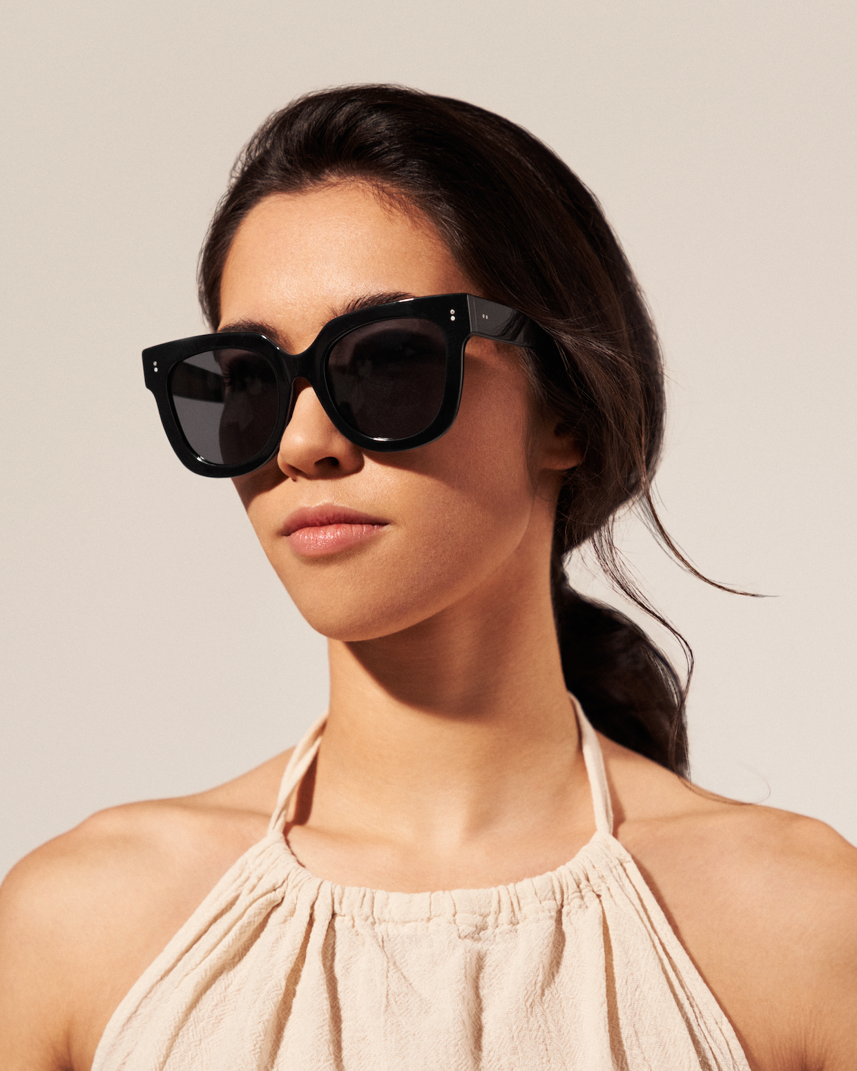 A woman in KayTran Eyewears Rowan - Polished Black sunglasses and a light halter top looks ahead.