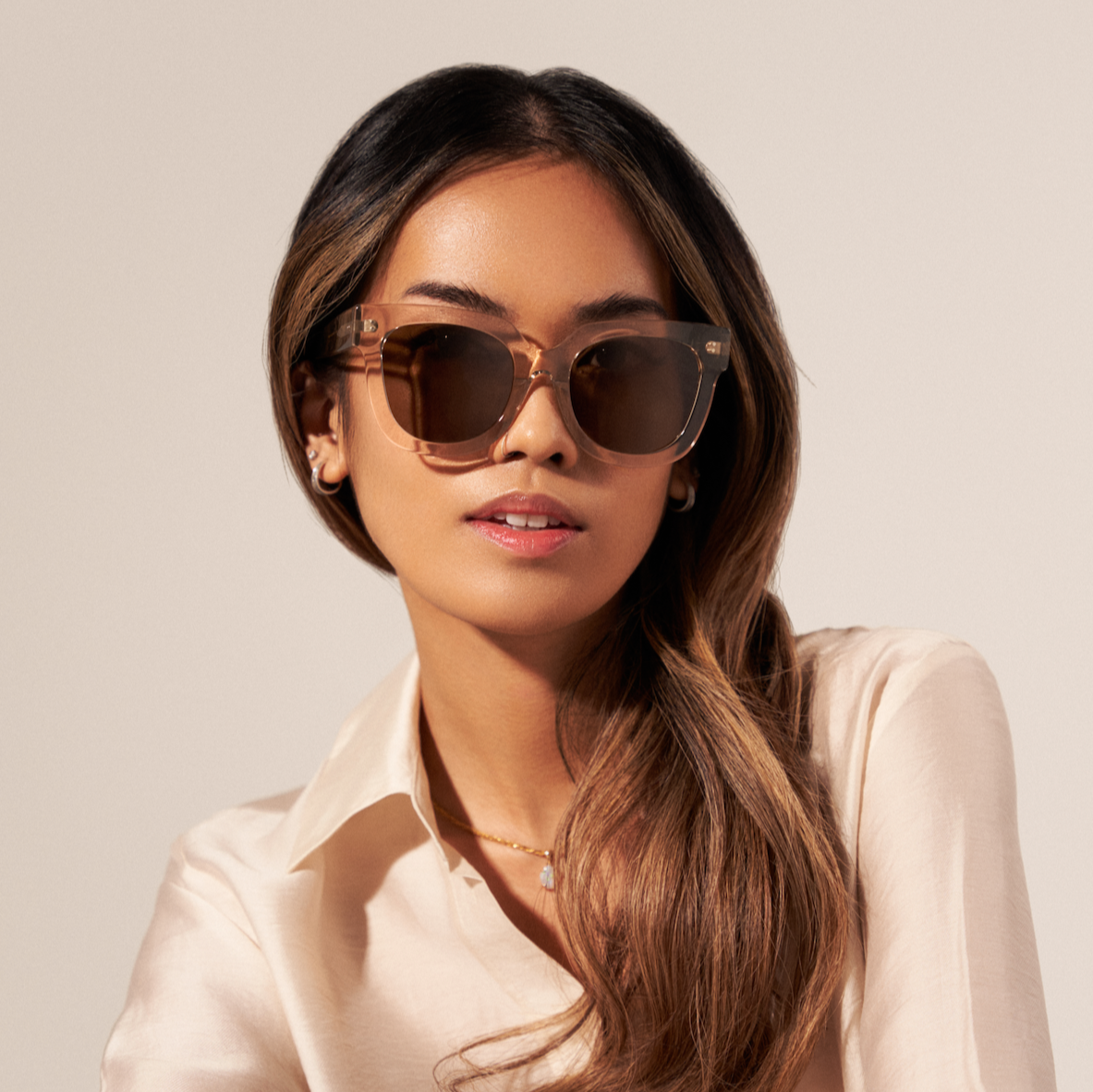 Woman wearing KayTran Eyewear’s Rowan - Sand sunglasses and a cream button-up shirt, hair over one shoulder.