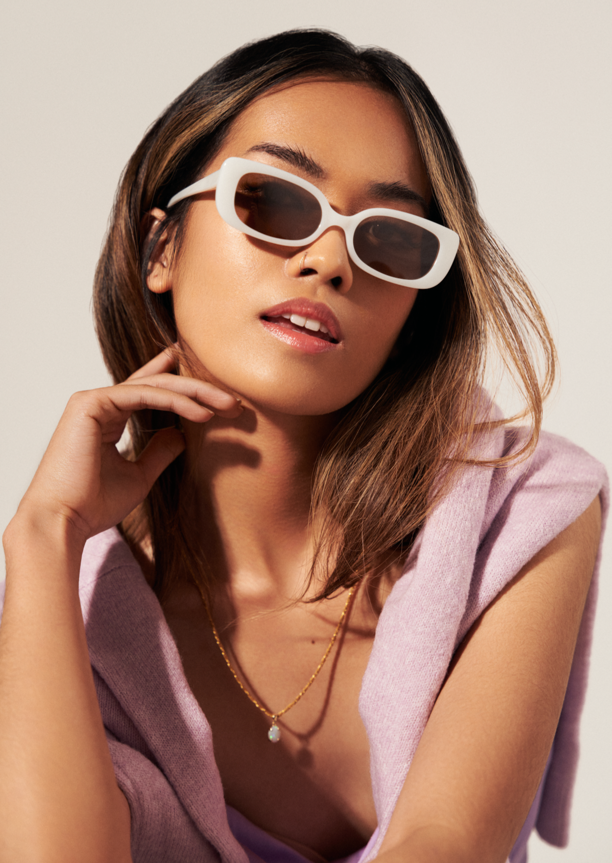 Woman wearing KayTran Eyewears Billie - Ivory sunglasses and a lavender top poses with one hand near her face.