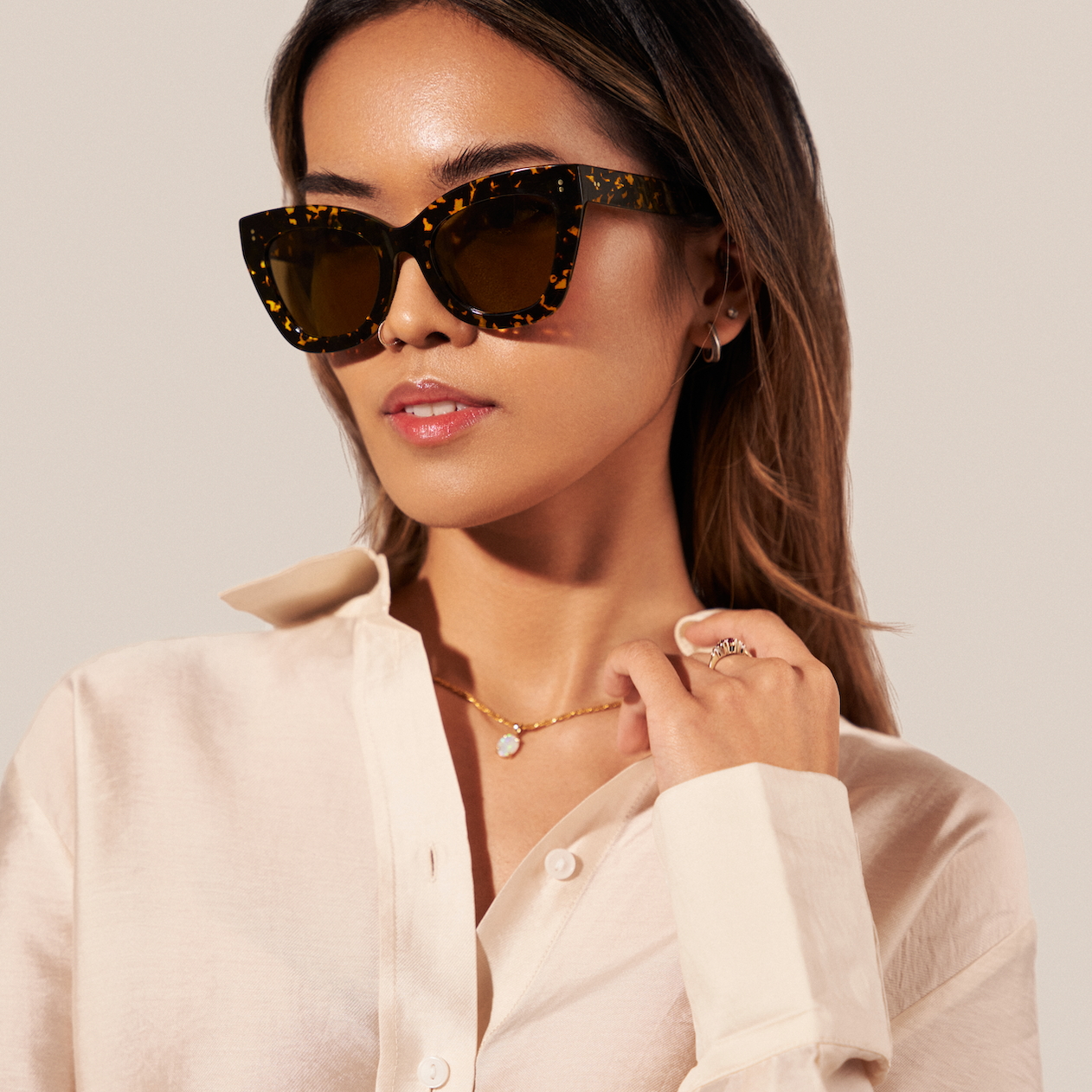 Woman wearing KayTran Eyewear’s Arlo - Amber Scale Tort sunglasses, cream shirt, gold jewelry, and a pearl necklace.