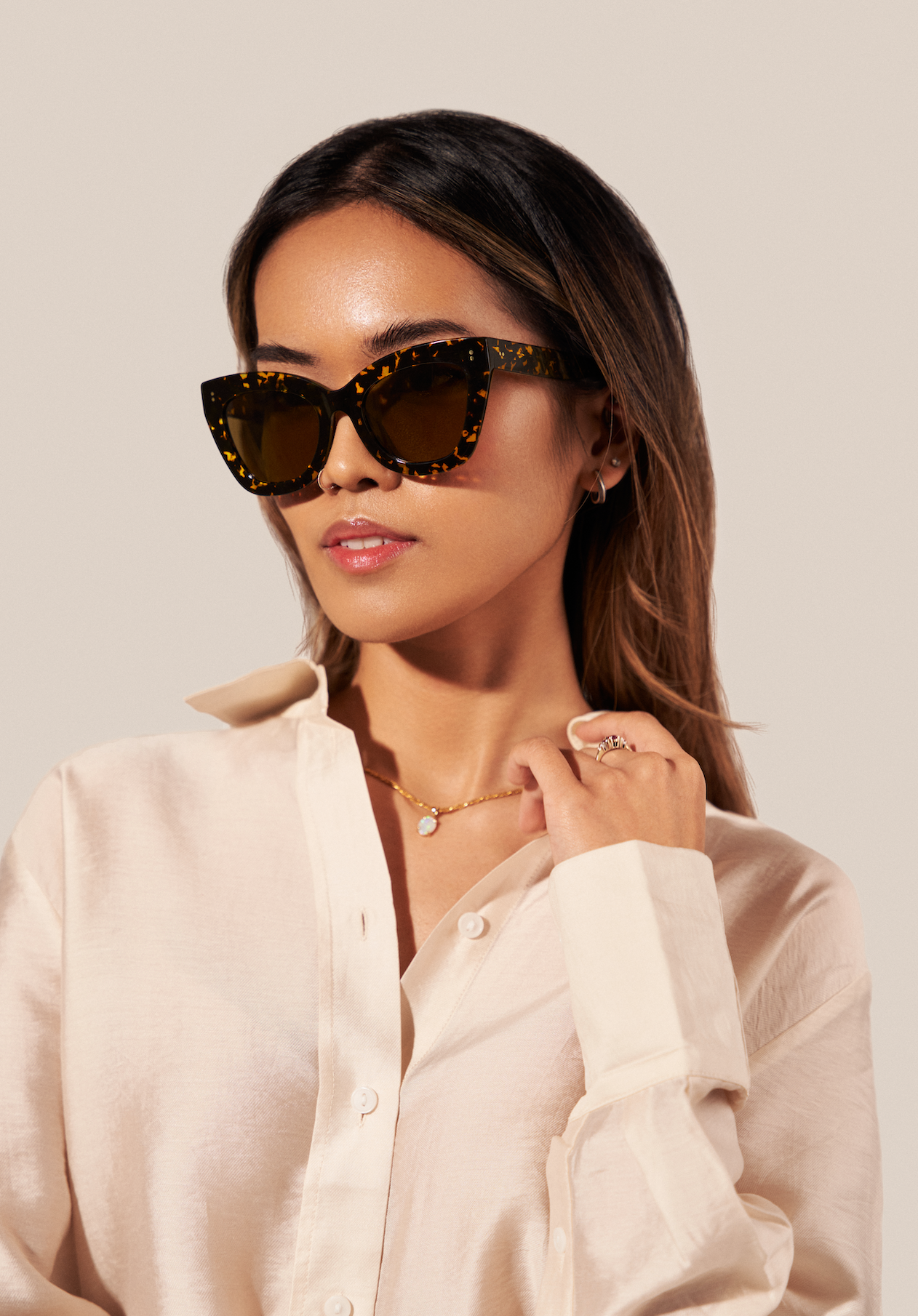 Woman wearing KayTran Eyewear’s Arlo - Amber Scale Tort sunglasses, cream shirt, gold jewelry, and a pearl necklace.