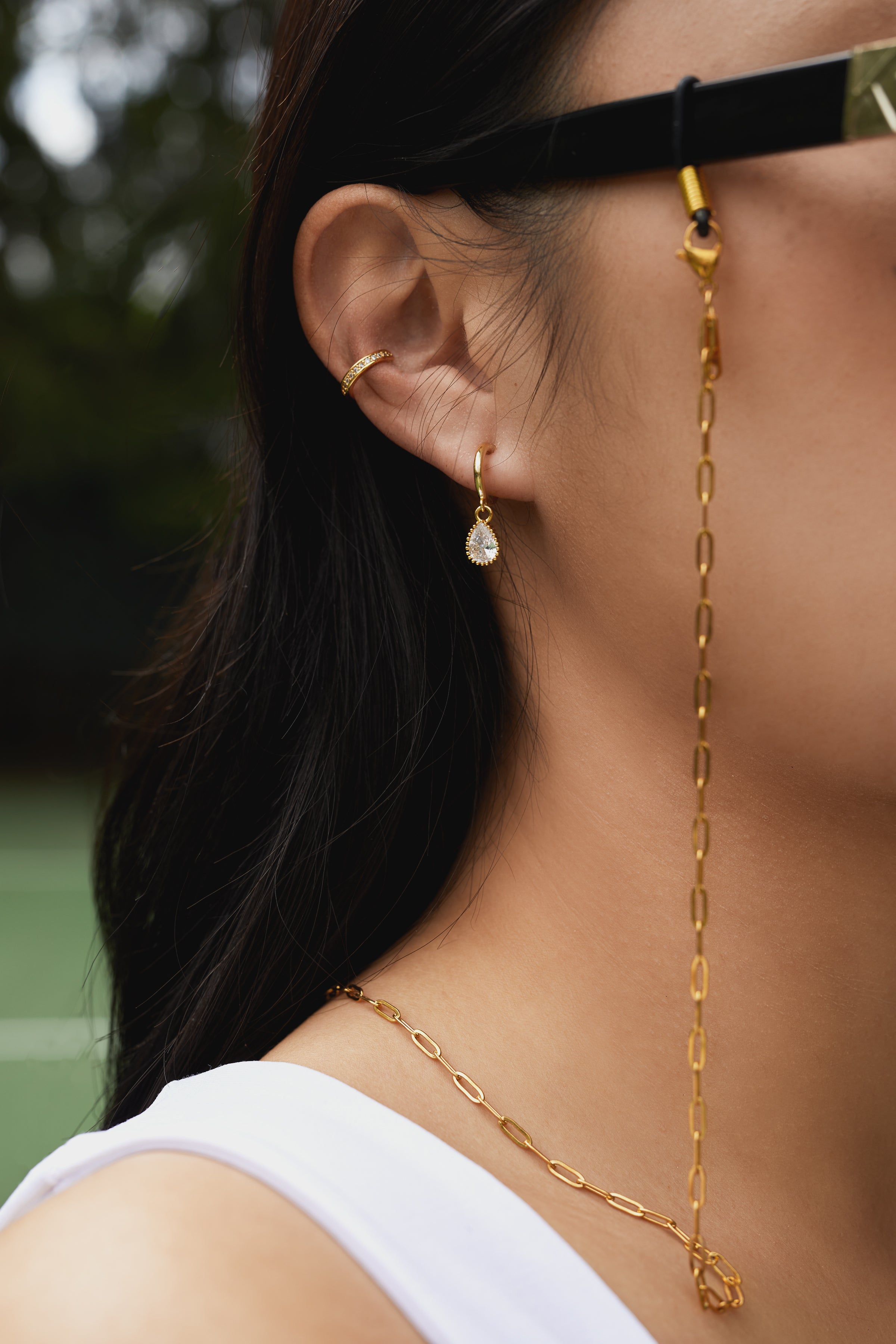 Close-up of a person wearing gold jewelry and glasses with the KayTran Eyewear Chain (KayTran x Aiori).