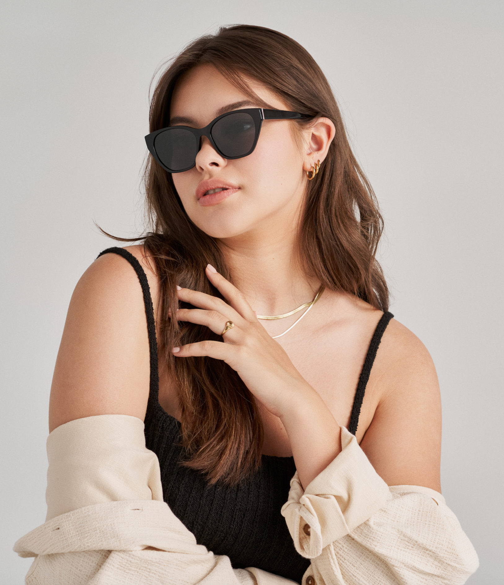 Woman wears KayTran Eyewears Taylor - Polished Black sunglasses, black top, gold jewelry, and beige sweater draped over shoulders.