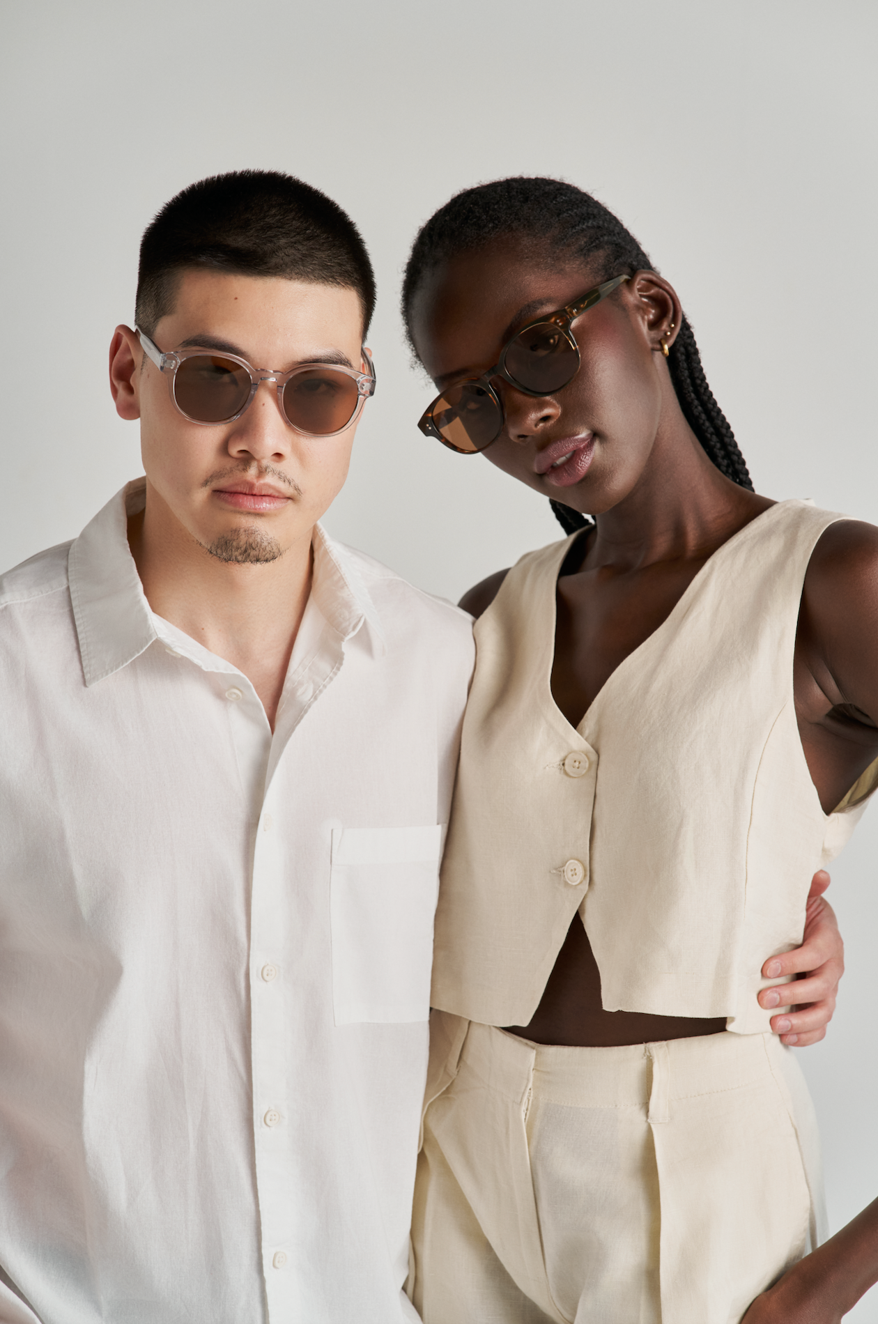 Two people wear KayTran Eyewears Reese - Amber Honey sunglasses, posing together in light, neutral outfits.