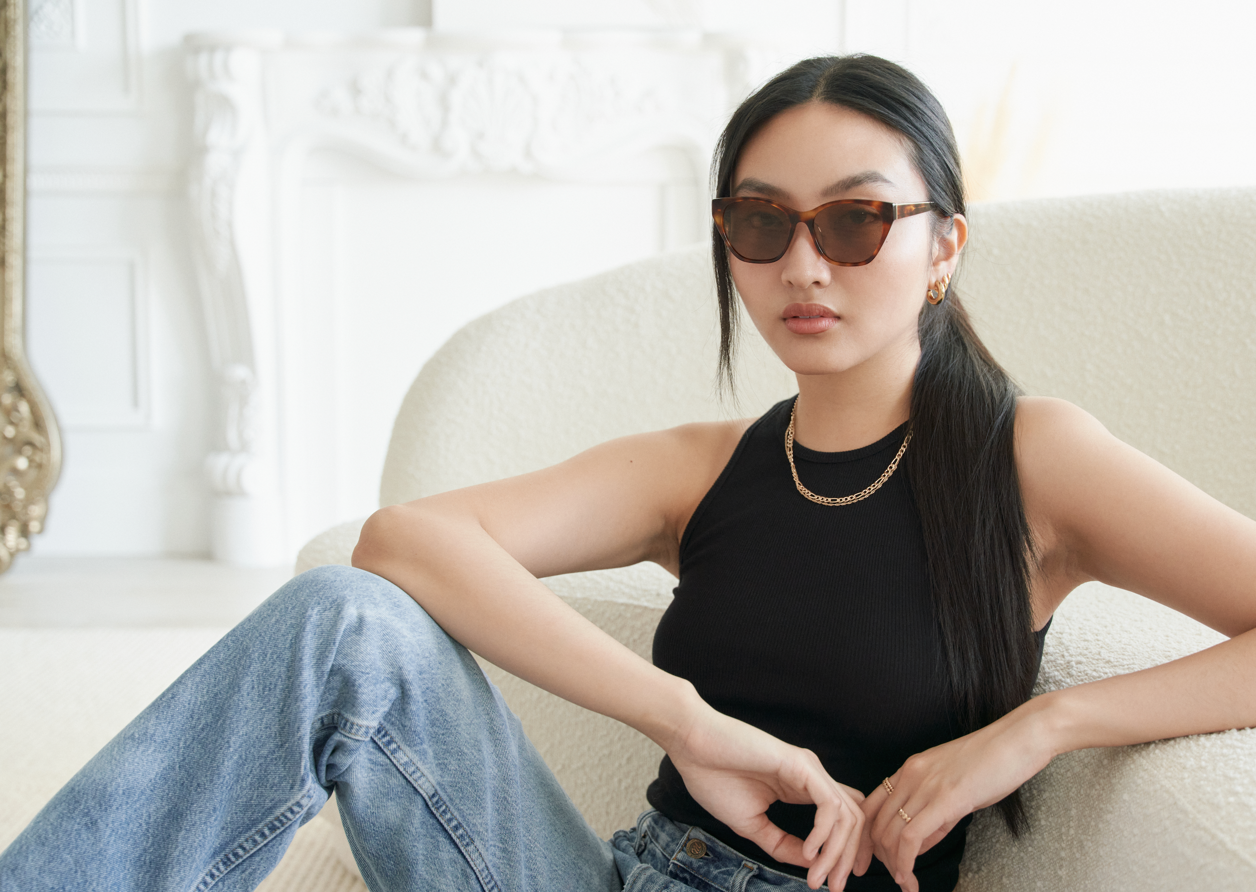 A woman wearing KayTran Eyewears Taylor - Honey Tort glasses sits in a chair.