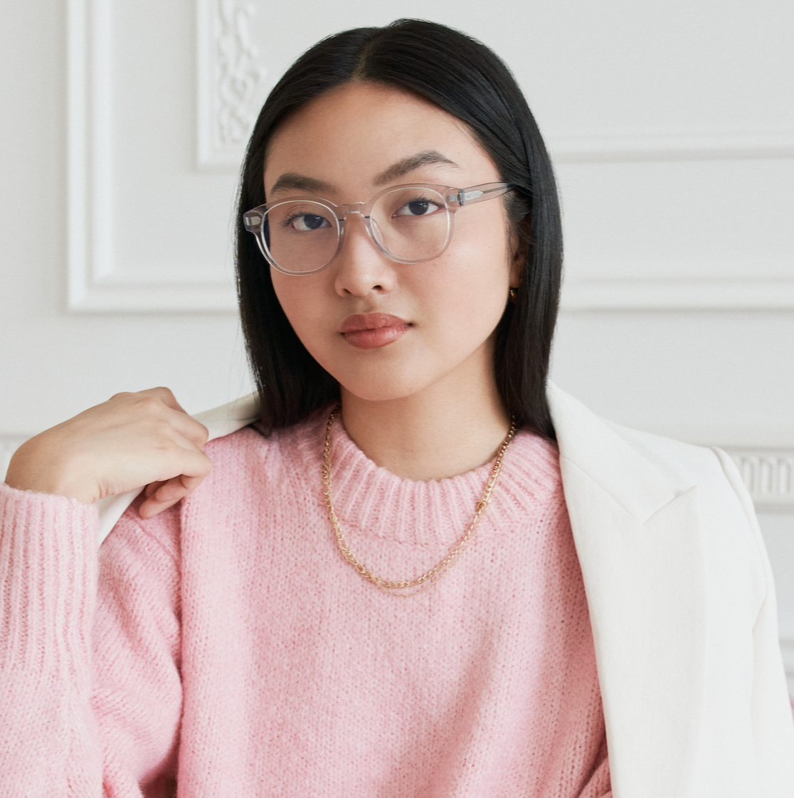 Woman with long black hair wears KayTran Eyewears Reese Optical - Fog glasses, pink sweater, and white blazer indoors.