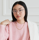 Woman with long black hair wears KayTran Eyewears Reese Optical - Fog glasses, pink sweater, and white blazer indoors.