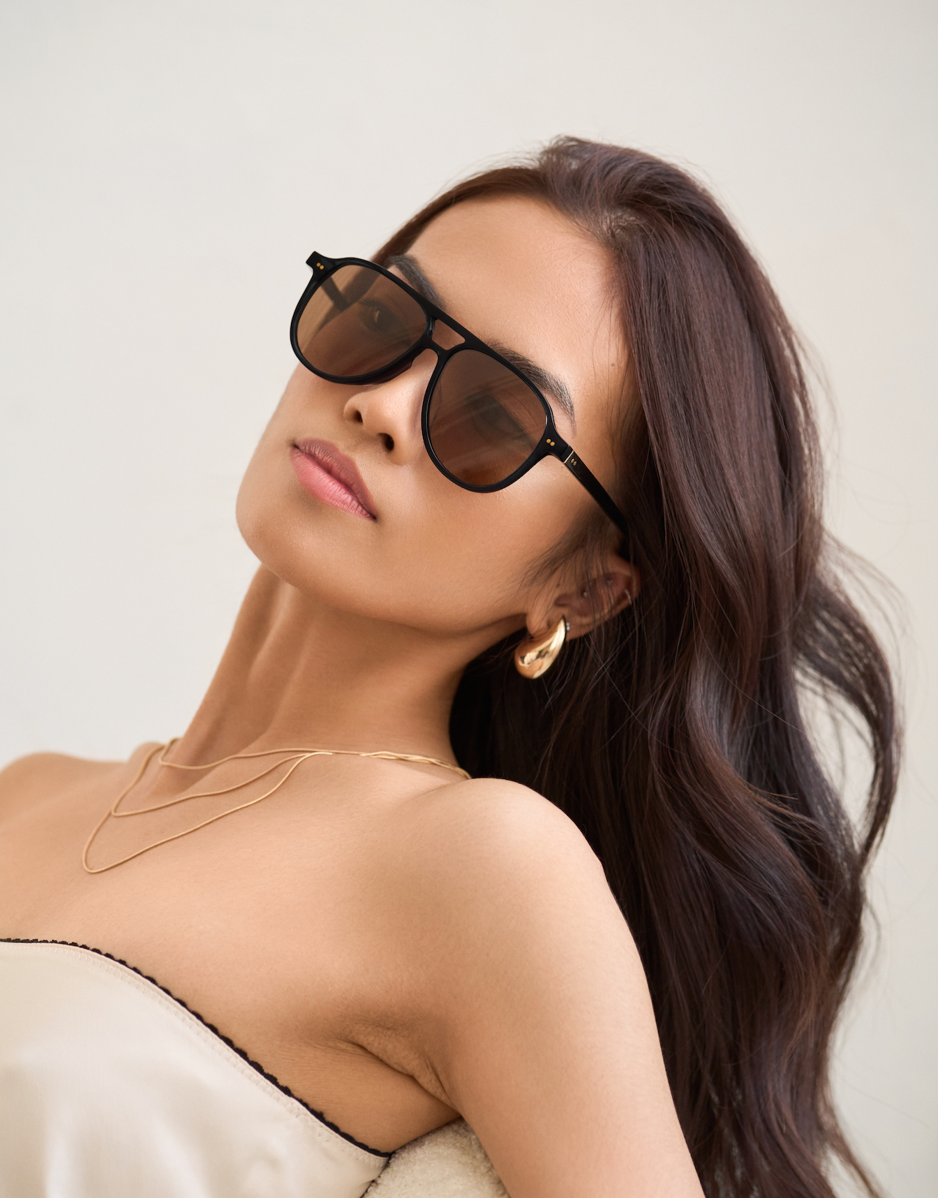 Woman with long brown hair wears KayTran Eyewears Knox - Black & Brown Lens sunglasses against a light background.