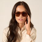 Woman with long dark hair wears KayTran Eyewears Knox - Cider sunglasses and a beige shirt against a neutral background.
