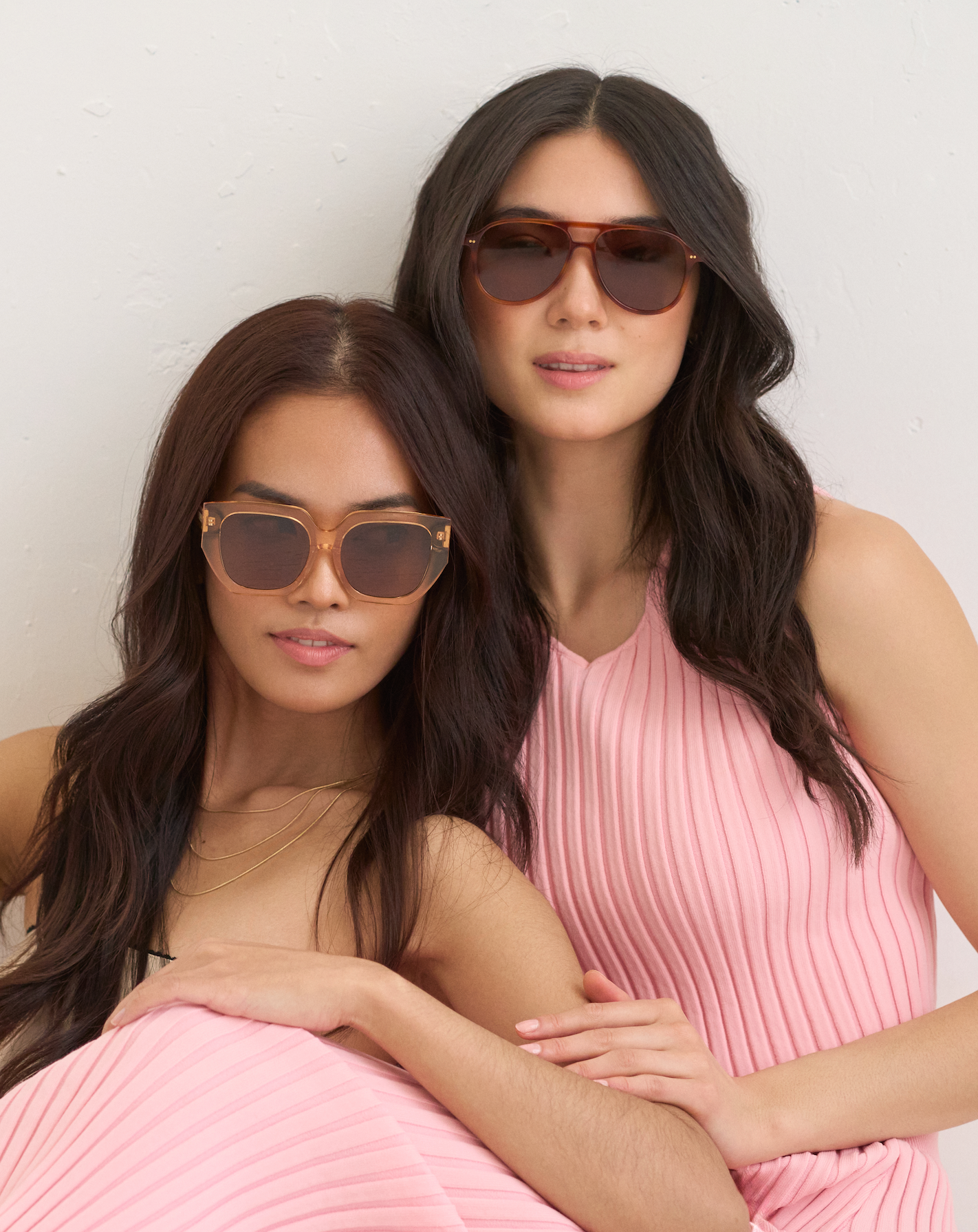 Two women wear KayTran Eyewears Luna - Apricot sunglasses and pink sleeveless dresses against a plain background.