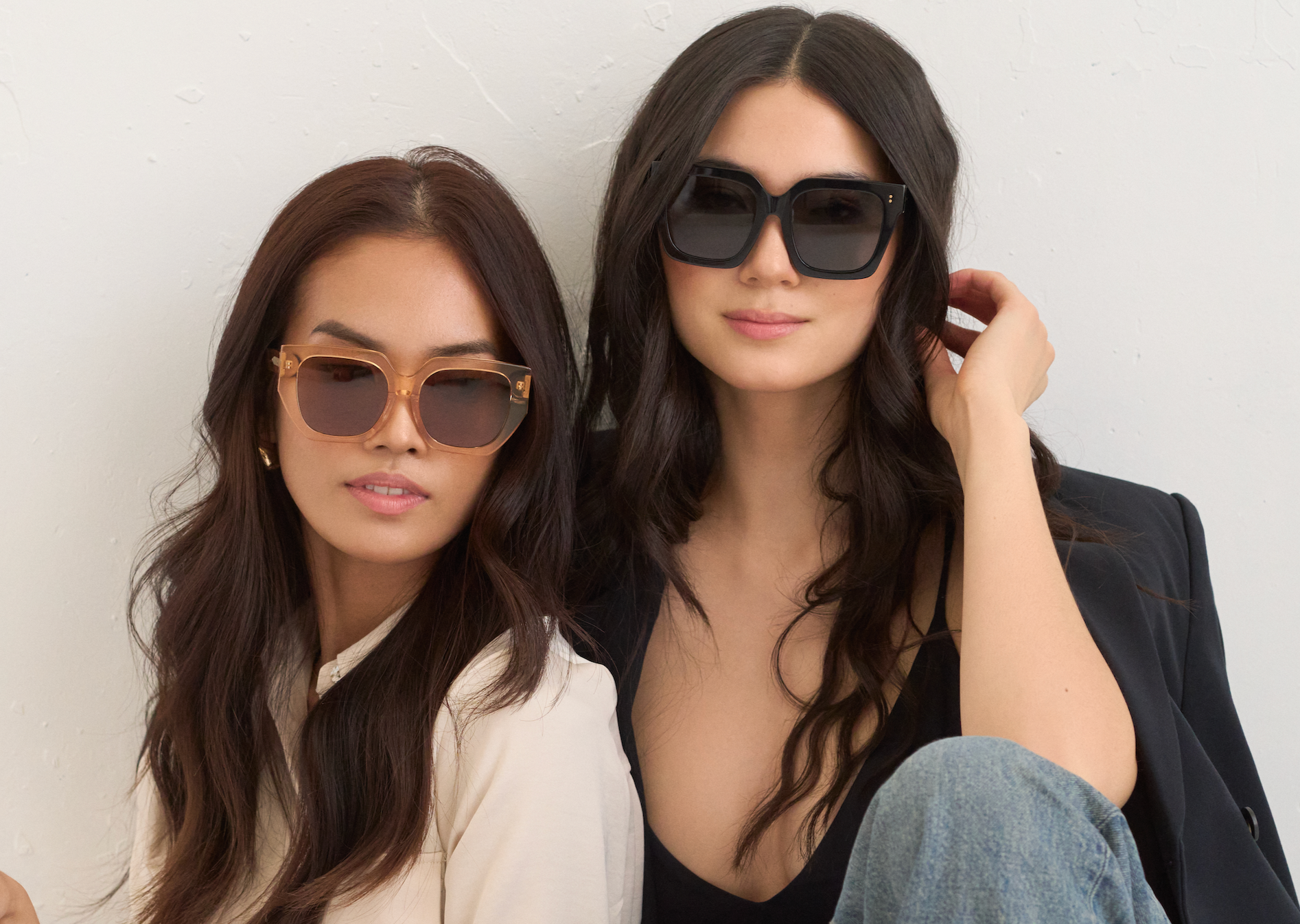 Two women wear KayTran Eyewears Luna - Apricot sunglasses, one in light, one in dark clothing against a bright backdrop.