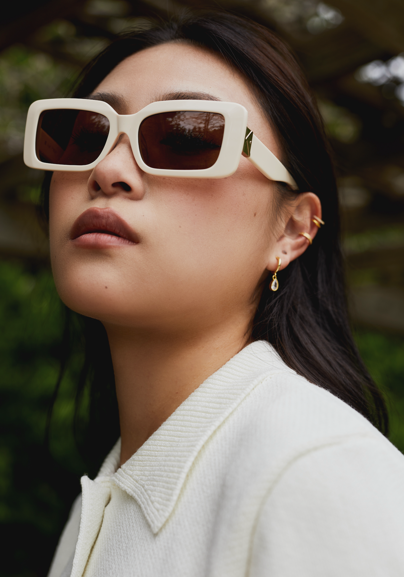 Woman wears Brooks - Ecru sunglasses by KayTran Eyewear and a white collared top, standing outdoors.