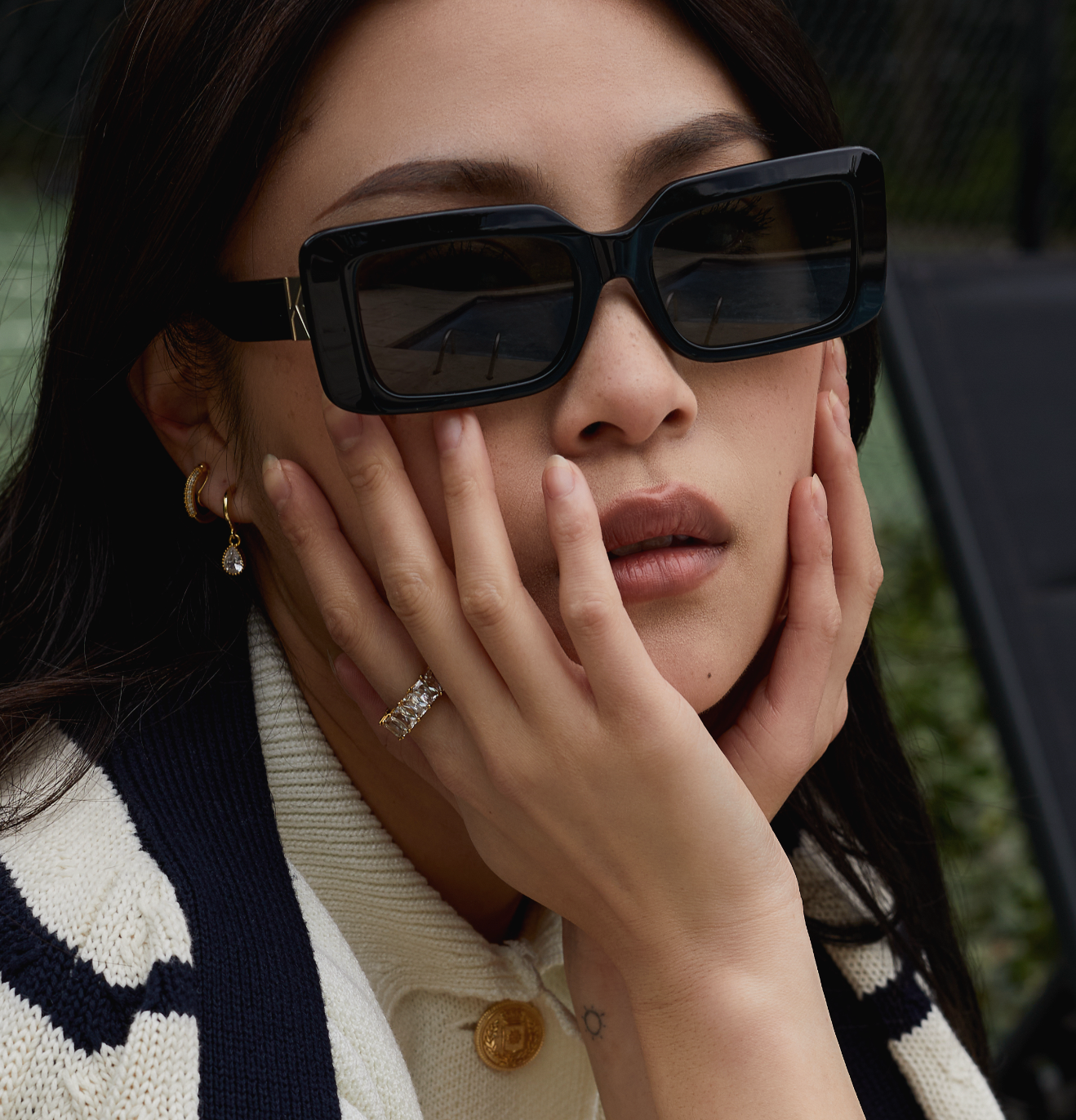 Woman wearing KayTran Eyewear Brooks - Polished Black sunglasses rests her face in her hands, gazing into the distance.