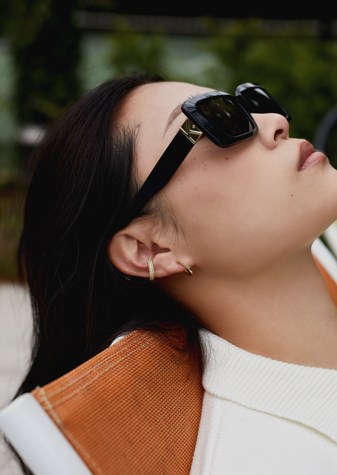 Woman wearing KayTran Eyewear Brooks - Polished Black sunglasses reclines on an orange lounge chair, gazing upward.