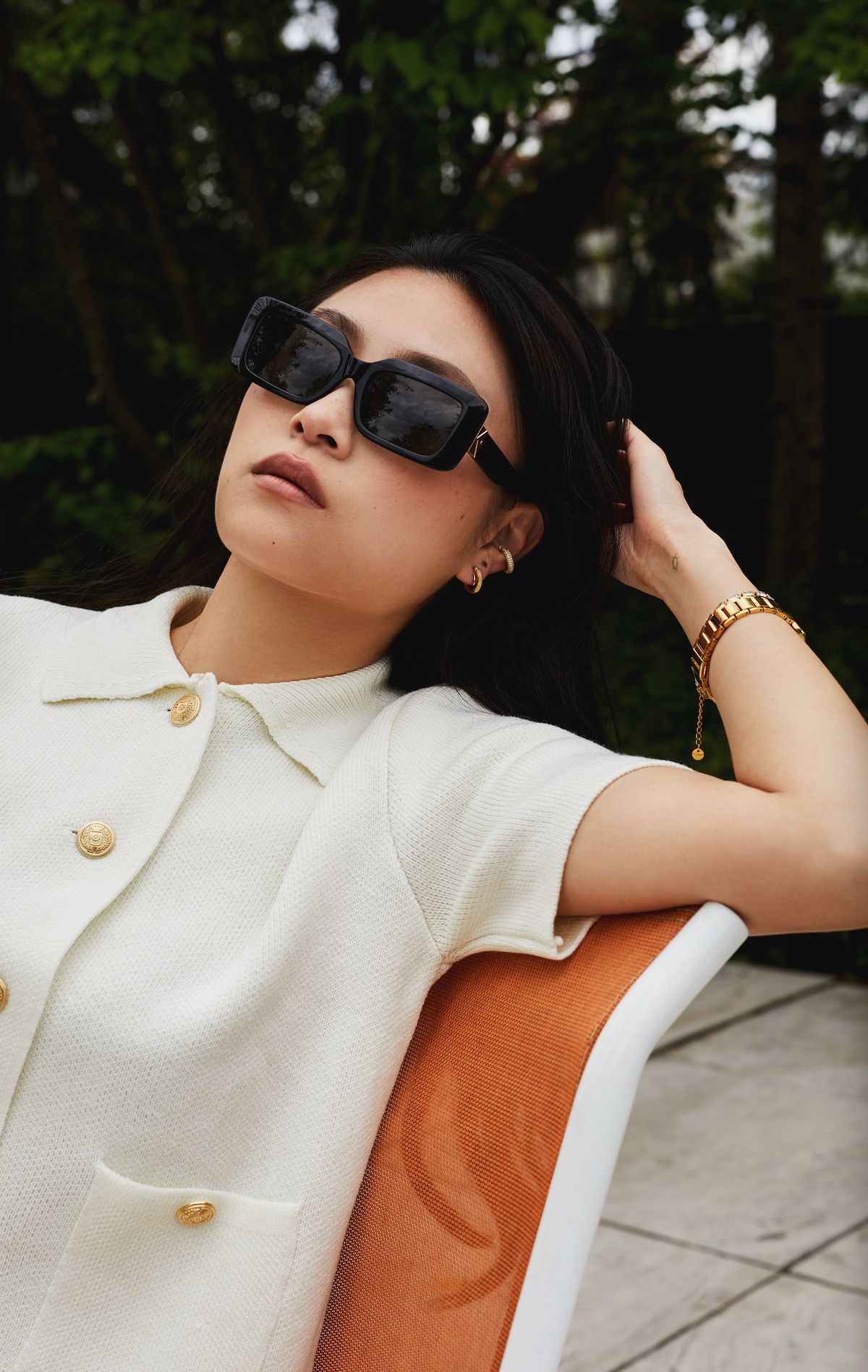 A woman wearing KayTran Eyewears Brooks - Polished Black sunglasses reclines on an orange chair outdoors.