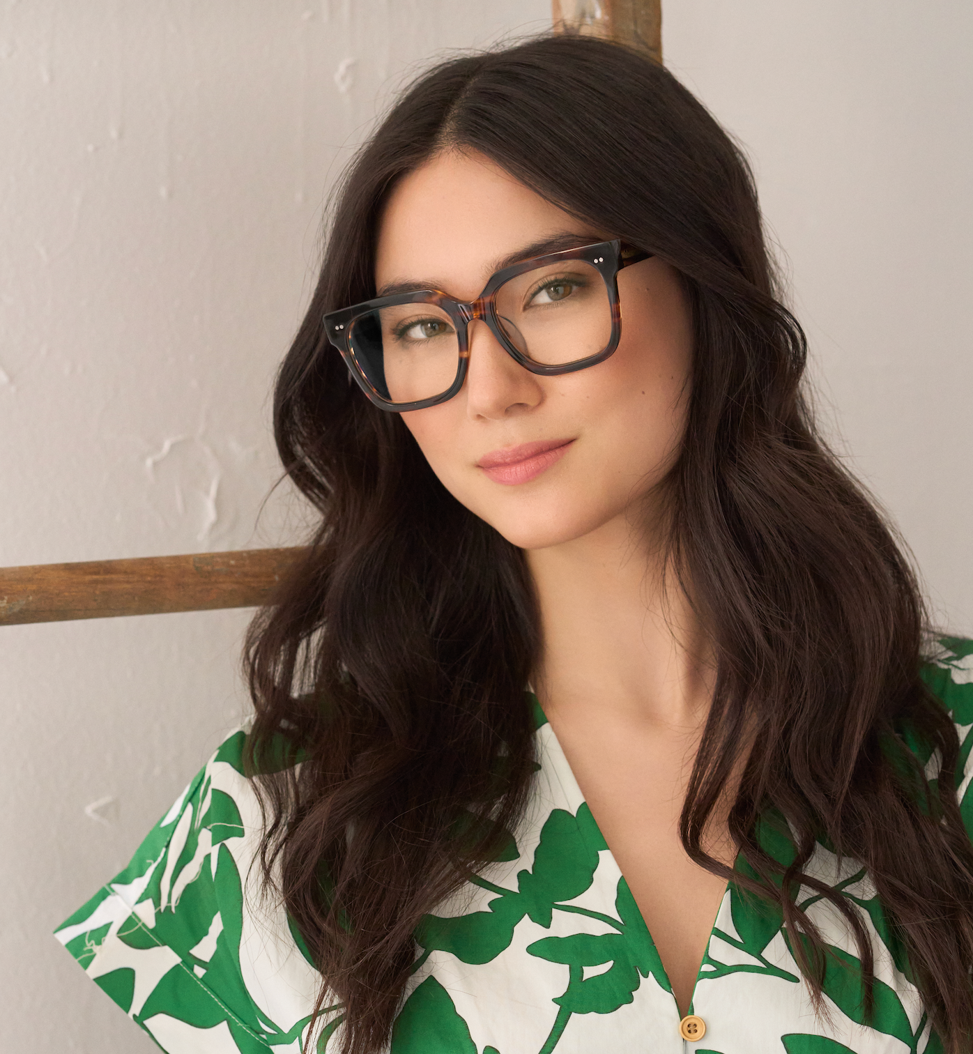 Woman with long dark hair wears KayTran Eyewears Andy - Amber Honey glasses, posed by a neutral wall.