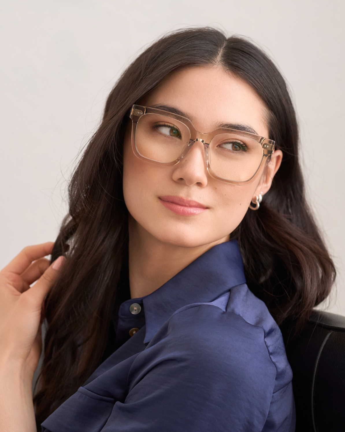 Woman with long dark hair wears KayTran Eyewears Andy - Sand glasses, seated and looking to the side.