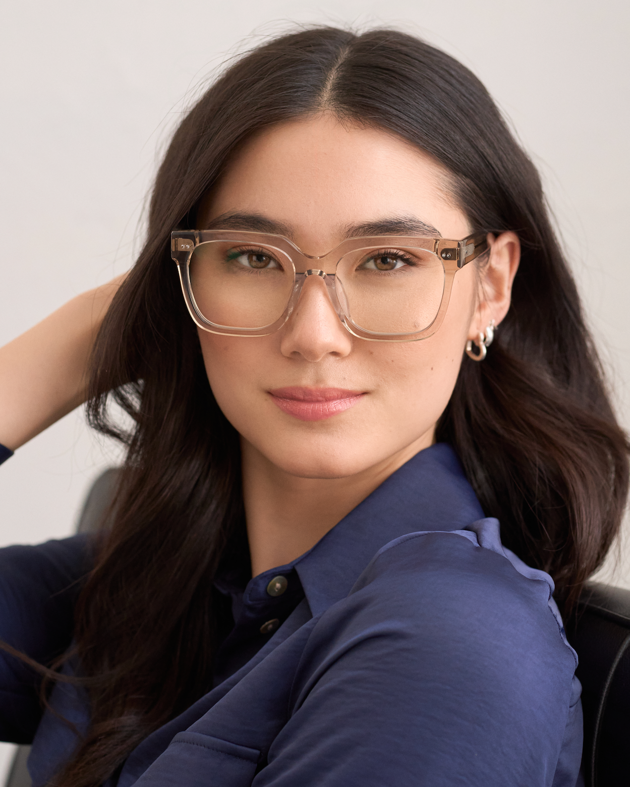 Woman with long dark hair wears KayTran Eyewears Andy - Sand glasses and a navy shirt, looking at the camera.