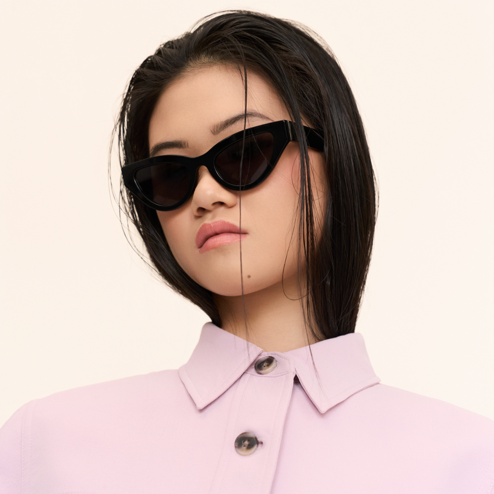 A woman with straight dark hair wears KayTran Eyewears Drew - Polished Black sunglasses and a light pink collared shirt.
