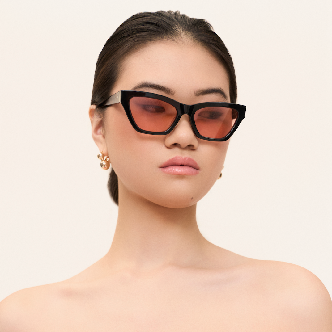 Woman wears KayTran Eyewears Kai - Black and Peach *Limited Edition* sunglasses, gazing sideways against a plain background.