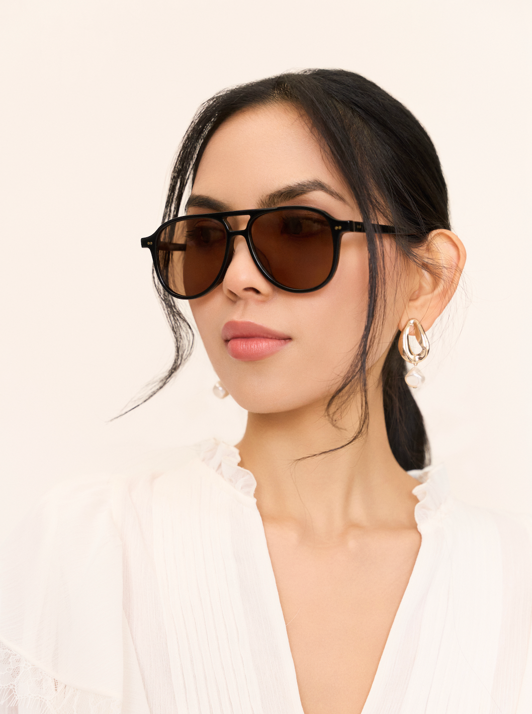 Woman in Knox - Black & Brown Lens by KayTran Eyewear, pearl drop earrings, white blouse, against a plain background.