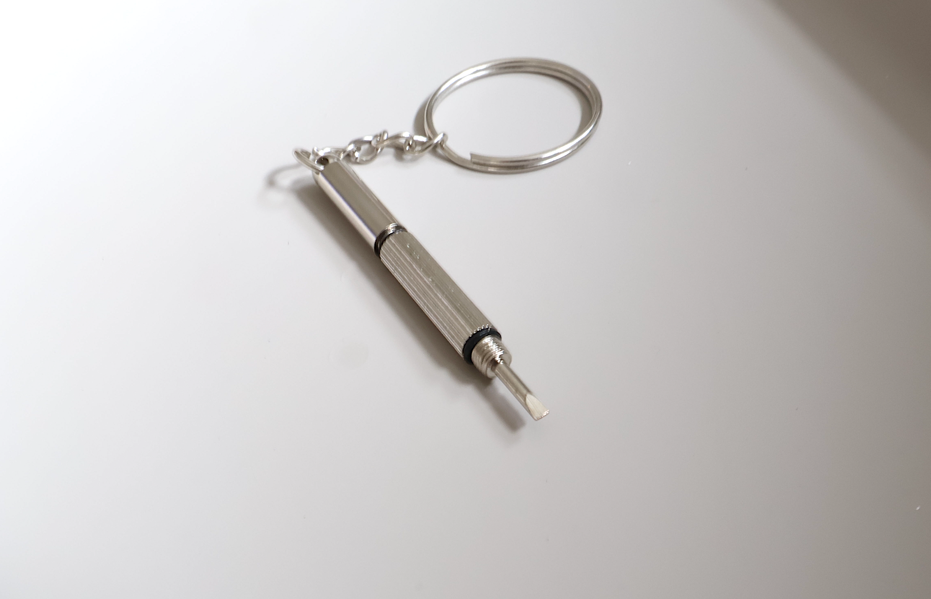 The KayTran Eyewear Tune Up Kit flathead screwdriver keychain rests on white, attached to a metal keyring.