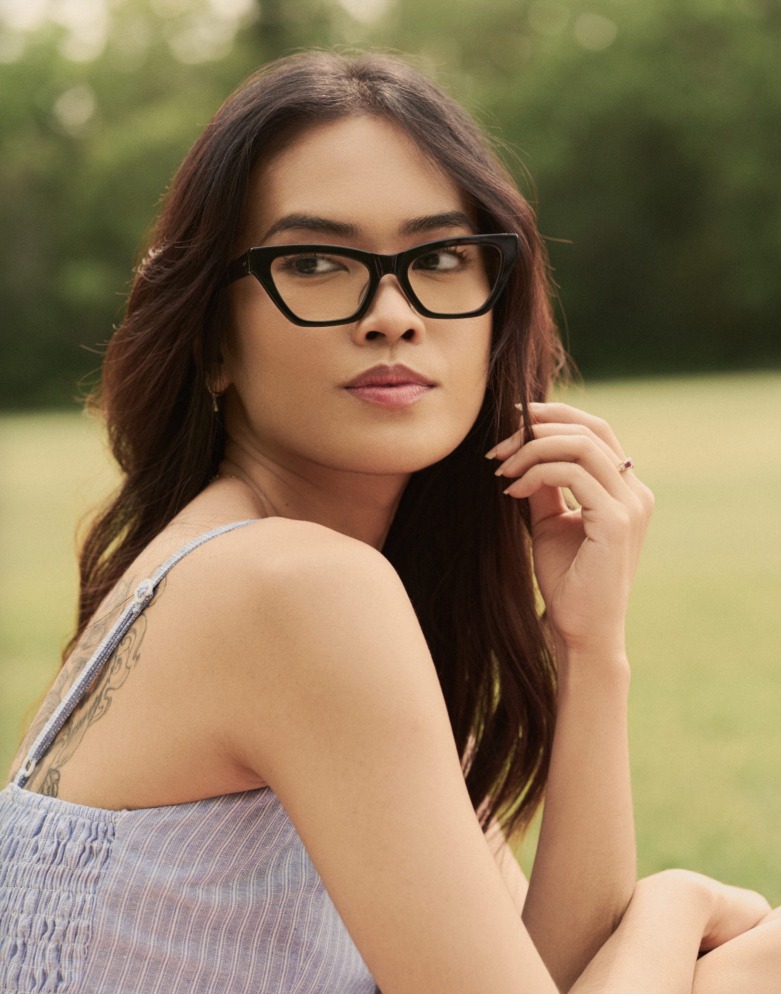 A woman wears KayTran Eyewears Kai Optical - Polished Black glasses outdoors with greenery in the background.