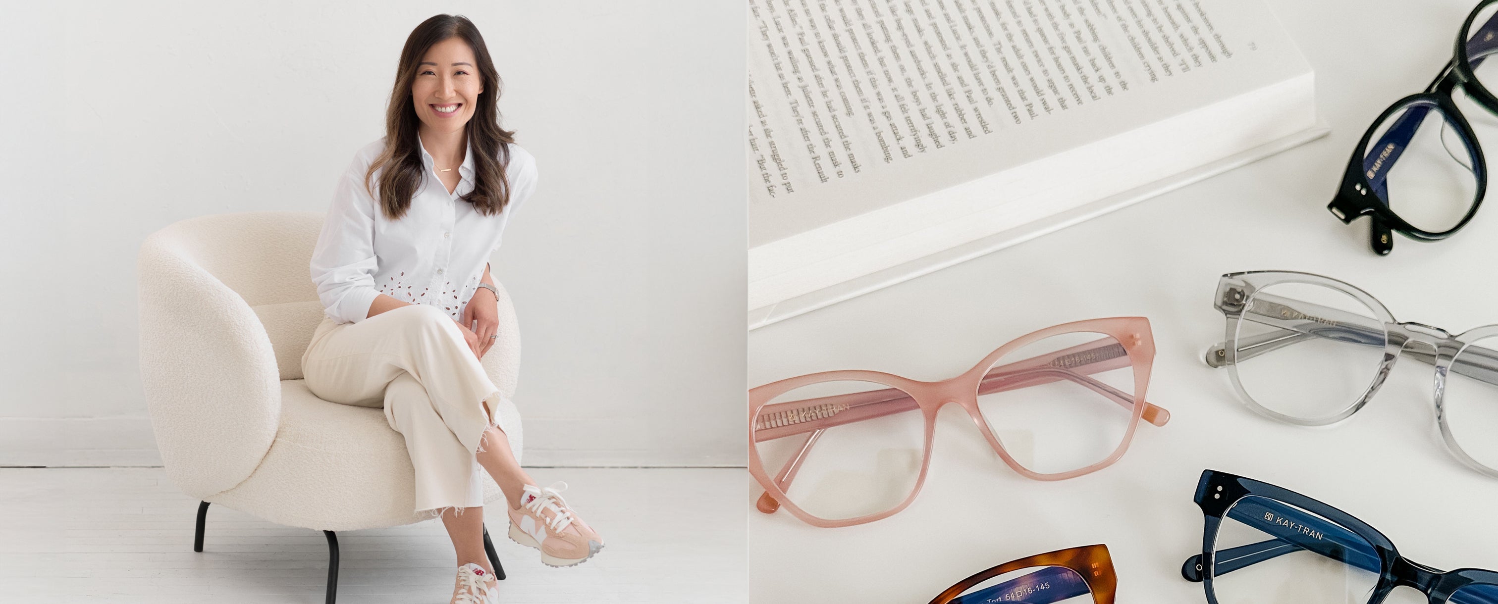 A woman sits on a white chair smiling; beside her are various eyeglasses and an open book on a white surface.