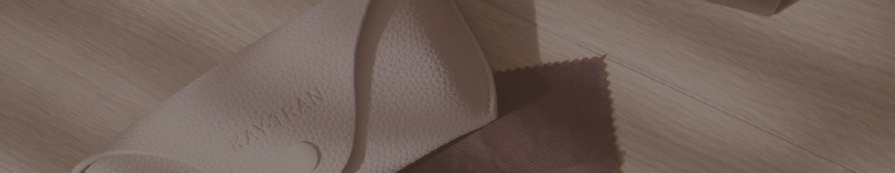 Close-up of a folded textured beige eyeglass case, a brown cleaning cloth, and a matching cylindrical container on wood.