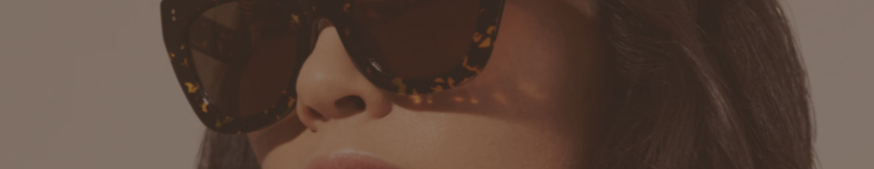Woman wearing large, dark tortoiseshell sunglasses with straight dark hair, shown from just below the eyes upward.
