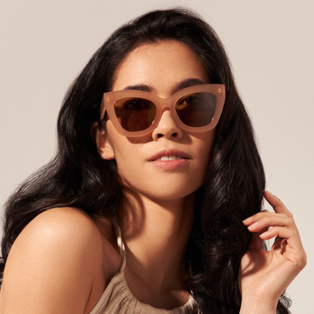 Woman with long dark hair wears KayTran Eyewears Arlo - Milky Blush cat-eye sunglasses, looking at the camera.